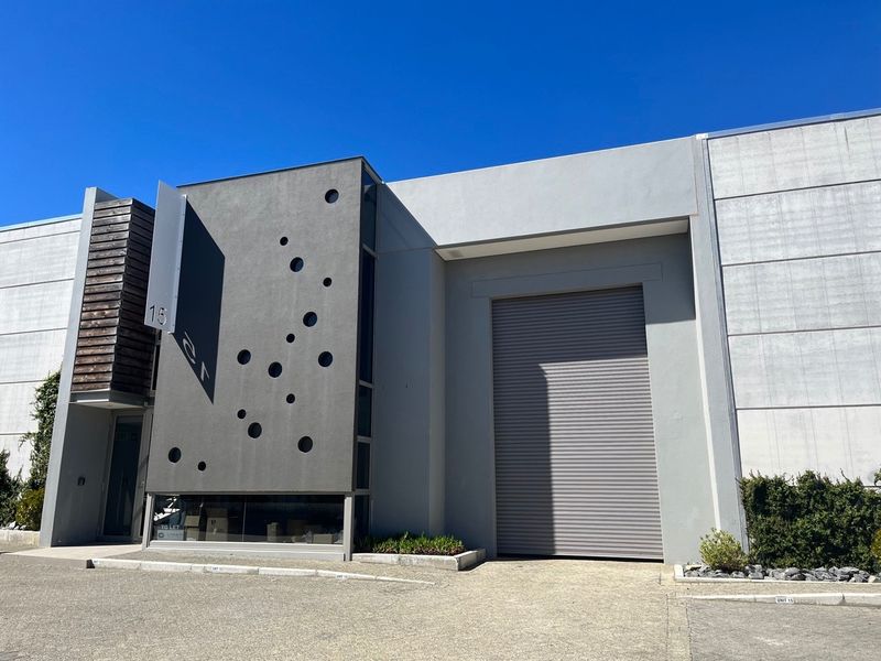 Modern industrial unit facade featuring a large roller shutter door, contemporary concrete finish with decorative circular accents, and timber cladding detail.