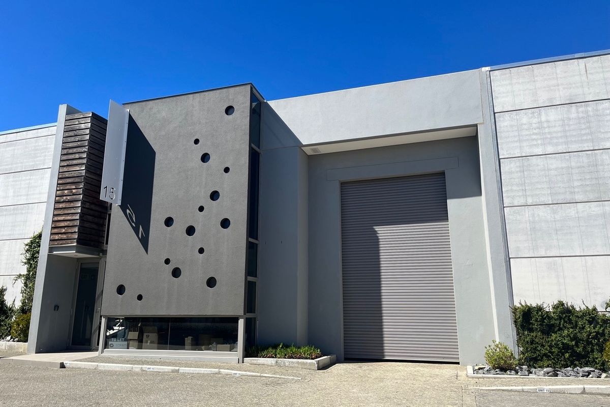 Modern industrial unit facade featuring a large roller shutter door, contemporary concrete finish with decorative circular accents, and timber cladding detail.