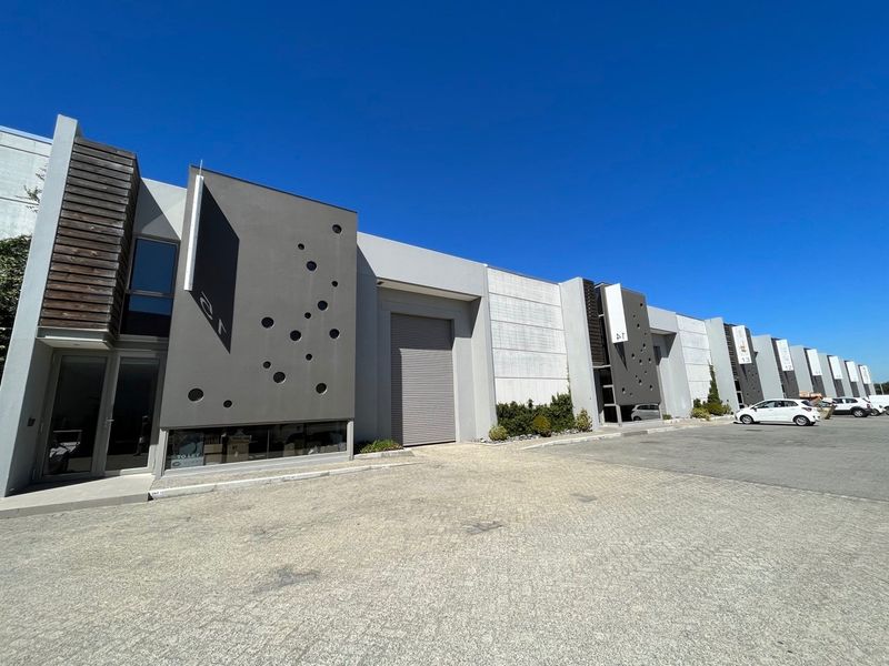 Modern industrial warehouse complex featuring a paved driveway, roller shutter doors, and contemporary architectural facade elements with decorative circular cutouts.