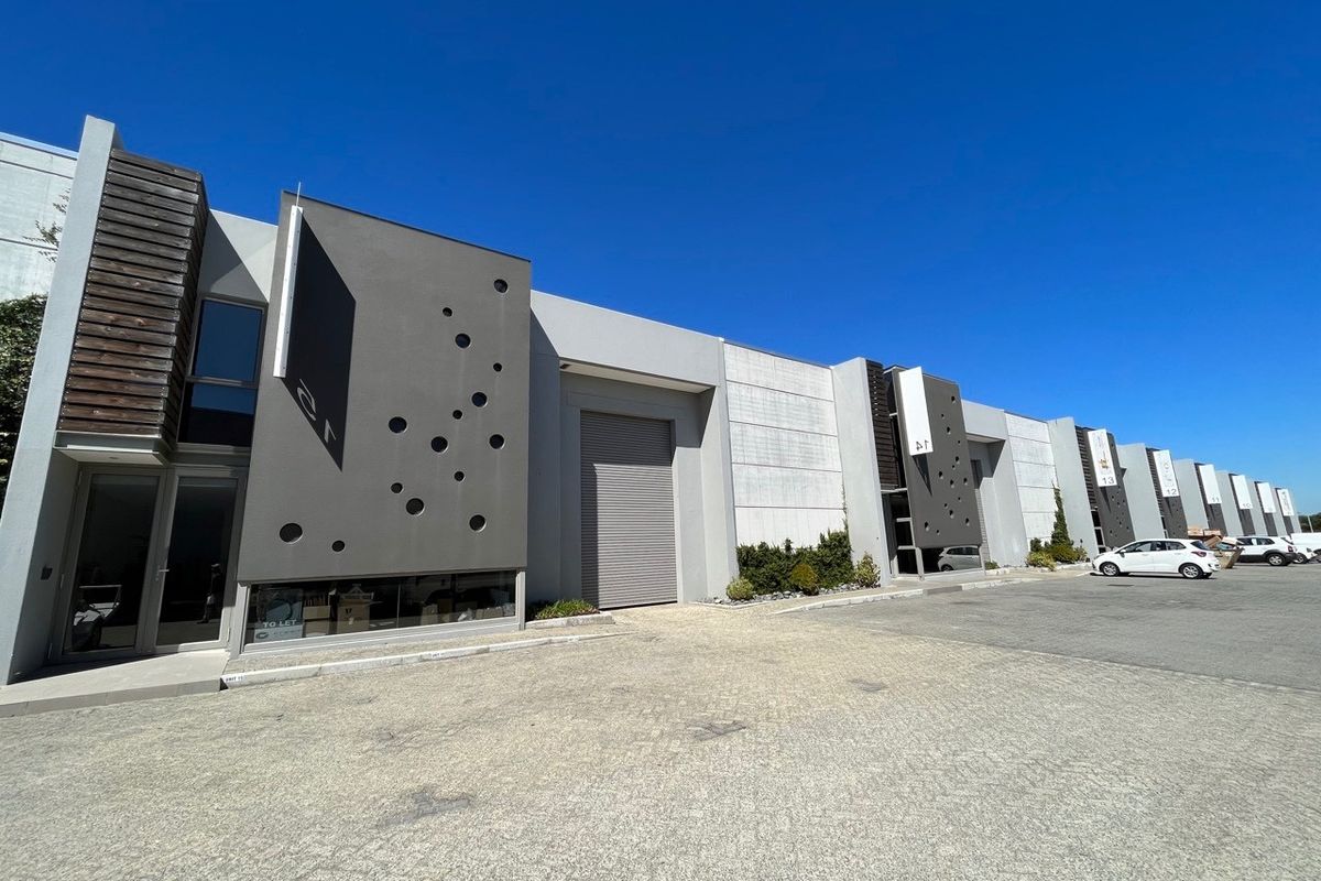 Modern industrial warehouse complex featuring a paved driveway, roller shutter doors, and contemporary architectural facade elements with decorative circular cutouts.