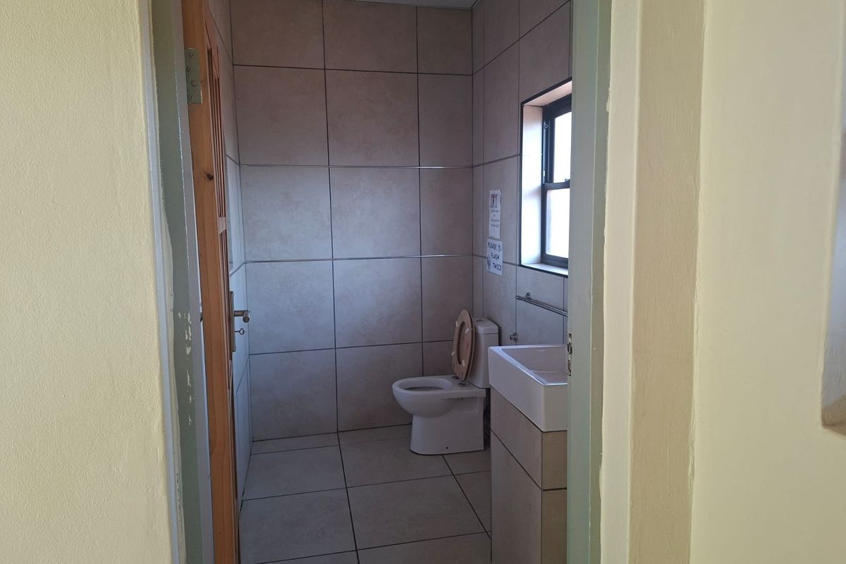 A functional office bathroom featuring tiled walls and flooring, a standard toilet, and a wall-mounted basin.