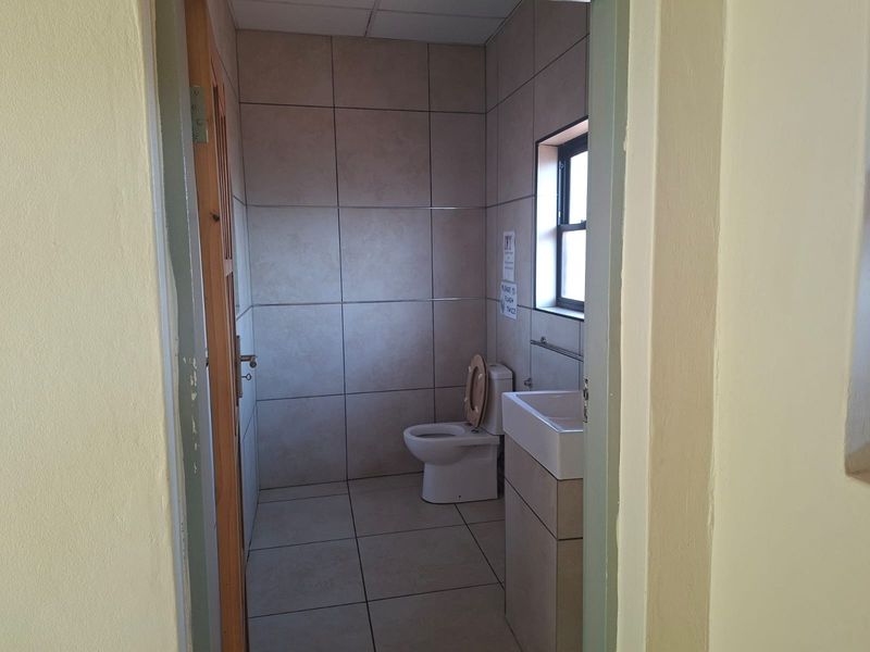 A functional office bathroom featuring tiled walls and flooring, a standard toilet, and a wall-mounted basin.