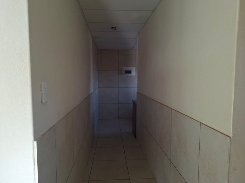 A narrow, tiled hallway featuring a drop ceiling and a wall-mounted electrical distribution board.