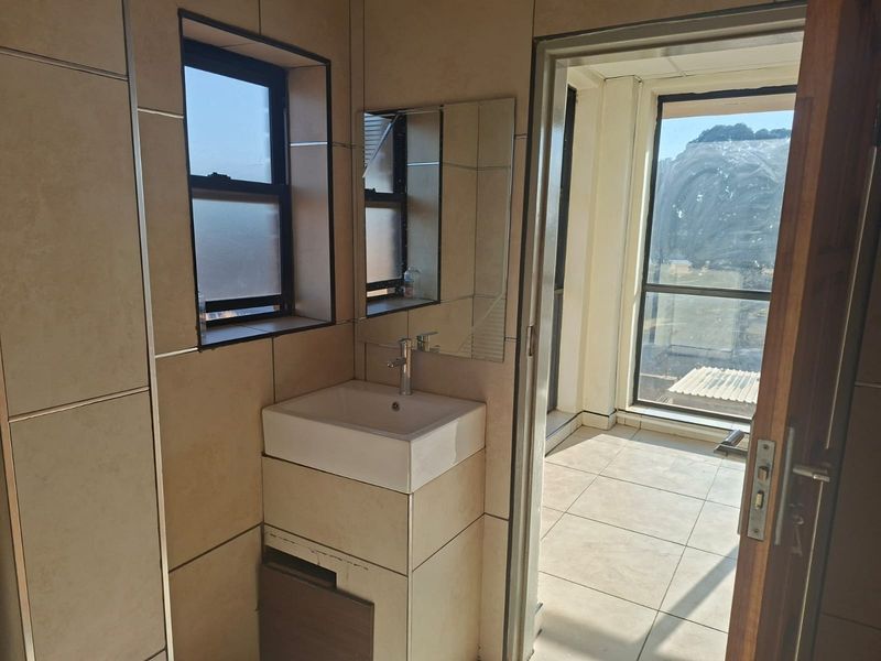 A compact bathroom featuring tiled walls and flooring, a modern vanity basin with a mixer tap, and a wall-mounted mirror.