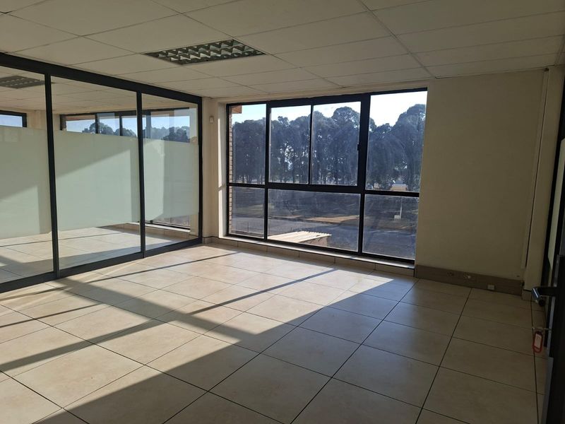 A bright, empty office space featuring large windows, tiled flooring, and a glass partition wall, suitable for a professional workspace.