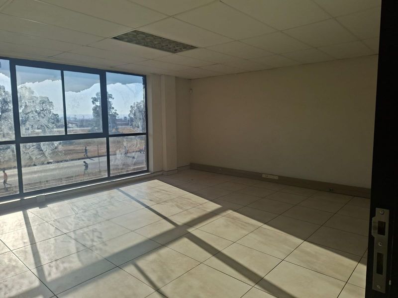 A vacant, sunlit office space featuring large windows, tiled flooring, and a suspended ceiling with recessed lighting, suitable for a professional workspace.