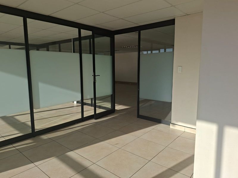 Empty office space featuring modern glass partitions, tiled flooring, and a suspended ceiling, offering a clean and professional environment.