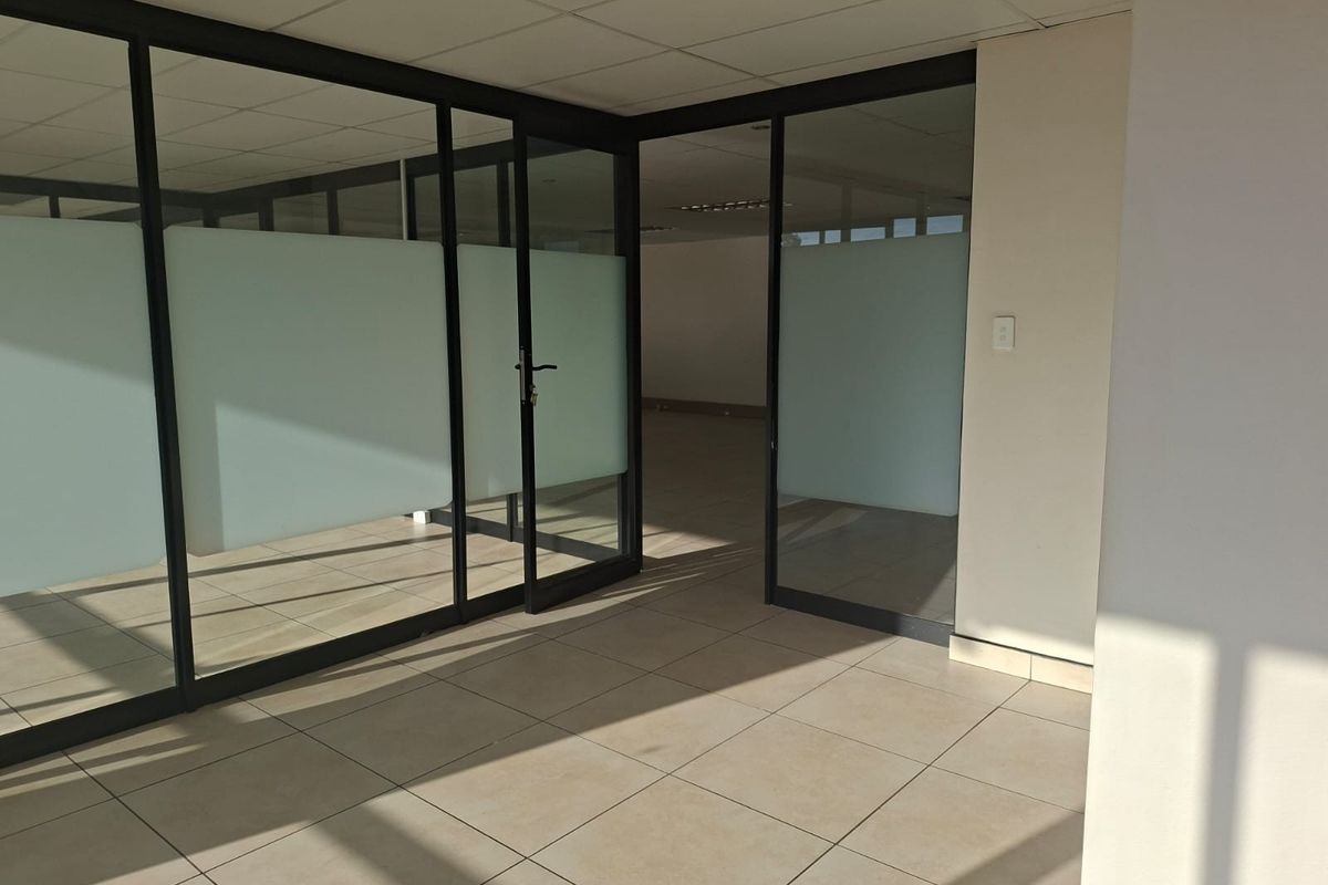 Empty office space featuring modern glass partitions, tiled flooring, and a suspended ceiling, offering a clean and professional environment.