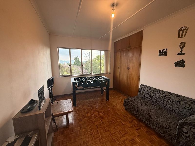 A bedroom featuring classic parquet flooring, built-in wooden cabinetry, and a large window providing natural light and exterior views.