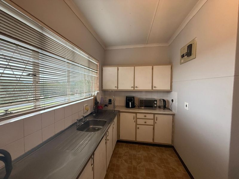 A functional kitchen featuring built-in cabinetry, laminate countertops, a stainless steel sink, and tiled backsplash, offering potential for a modern renovation.