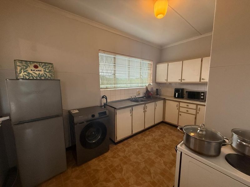A functional kitchen featuring laminate cabinetry, a stainless steel sink, tiled splashback, and vinyl flooring, offering potential for modernization.