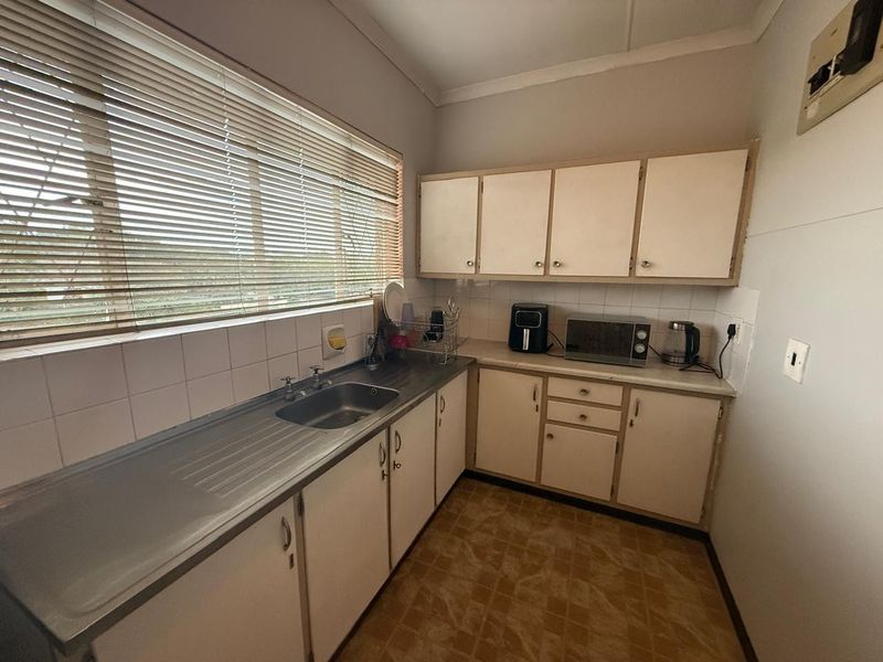 A functional kitchen featuring built-in cabinetry, a stainless steel sink, and tiled backsplash, offering a practical layout with potential for modern updates.