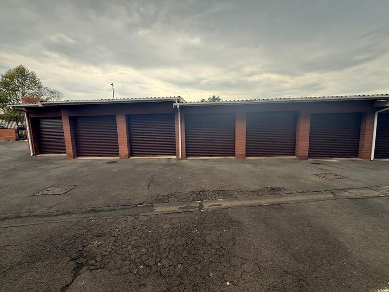 A row of secure brick-built garages featuring dark roller shutter doors and an asphalt driveway area.