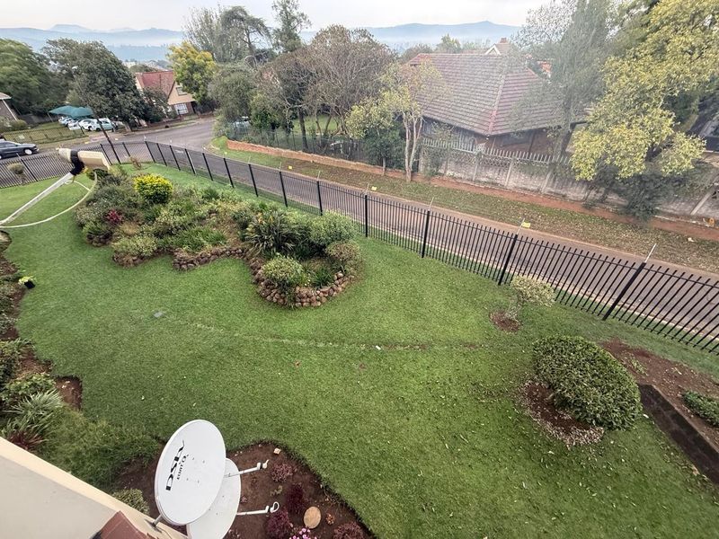 An elevated aerial view of a well-maintained residential garden featuring landscaped beds, a lawn, and secure metal perimeter fencing.