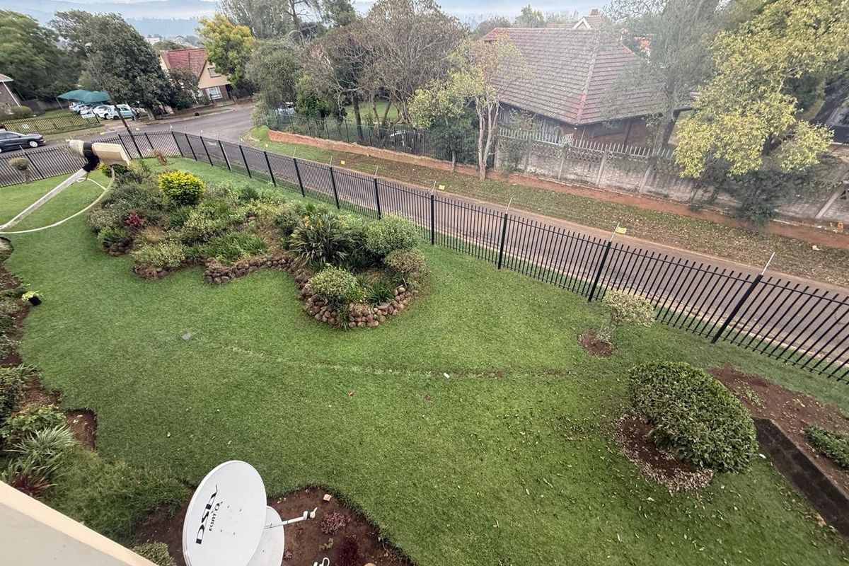 An elevated aerial view of a well-maintained residential garden featuring landscaped beds, a lawn, and secure metal perimeter fencing.