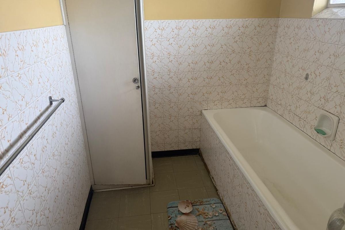 A dated bathroom featuring a standard bathtub, tiled walls, and floor, offering a blank canvas for a modern renovation.