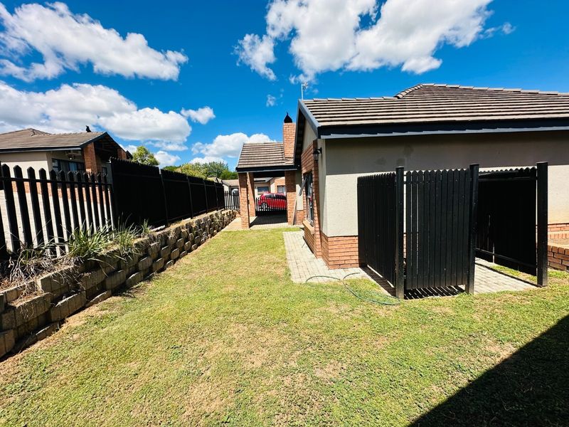 Rear exterior view of the property featuring a lawn, paved walkway, brick retaining wall, and secure perimeter fencing.