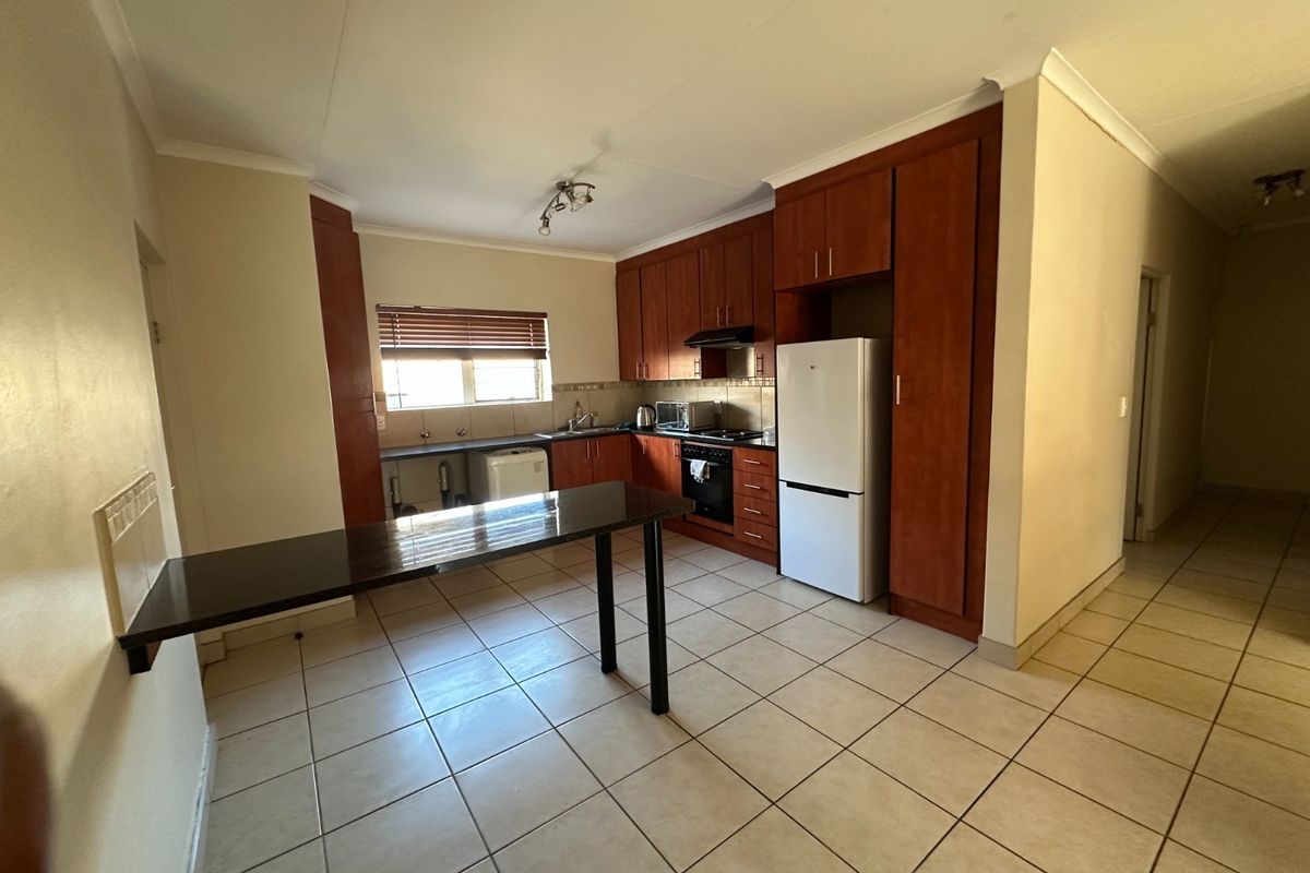 Functional kitchen featuring wooden cabinetry, built-in oven and hob, tiled flooring, and a convenient breakfast bar counter.