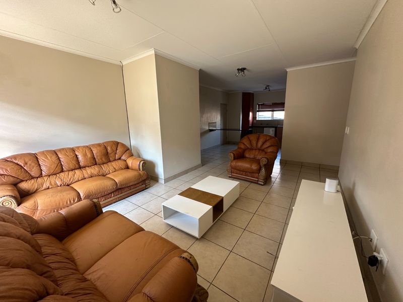 An open-plan living area featuring neutral wall tones, tiled flooring, and a coved ceiling, with a clear transition toward the kitchen space.