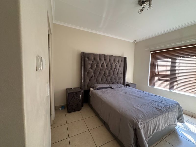 A functional bedroom featuring tiled flooring, neutral wall finishes, and venetian blinds for light control.