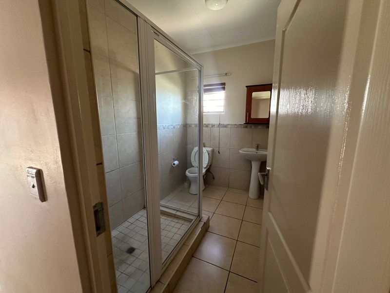 A functional bathroom featuring a glass-enclosed shower, pedestal sink, toilet, and neutral wall and floor tiling.