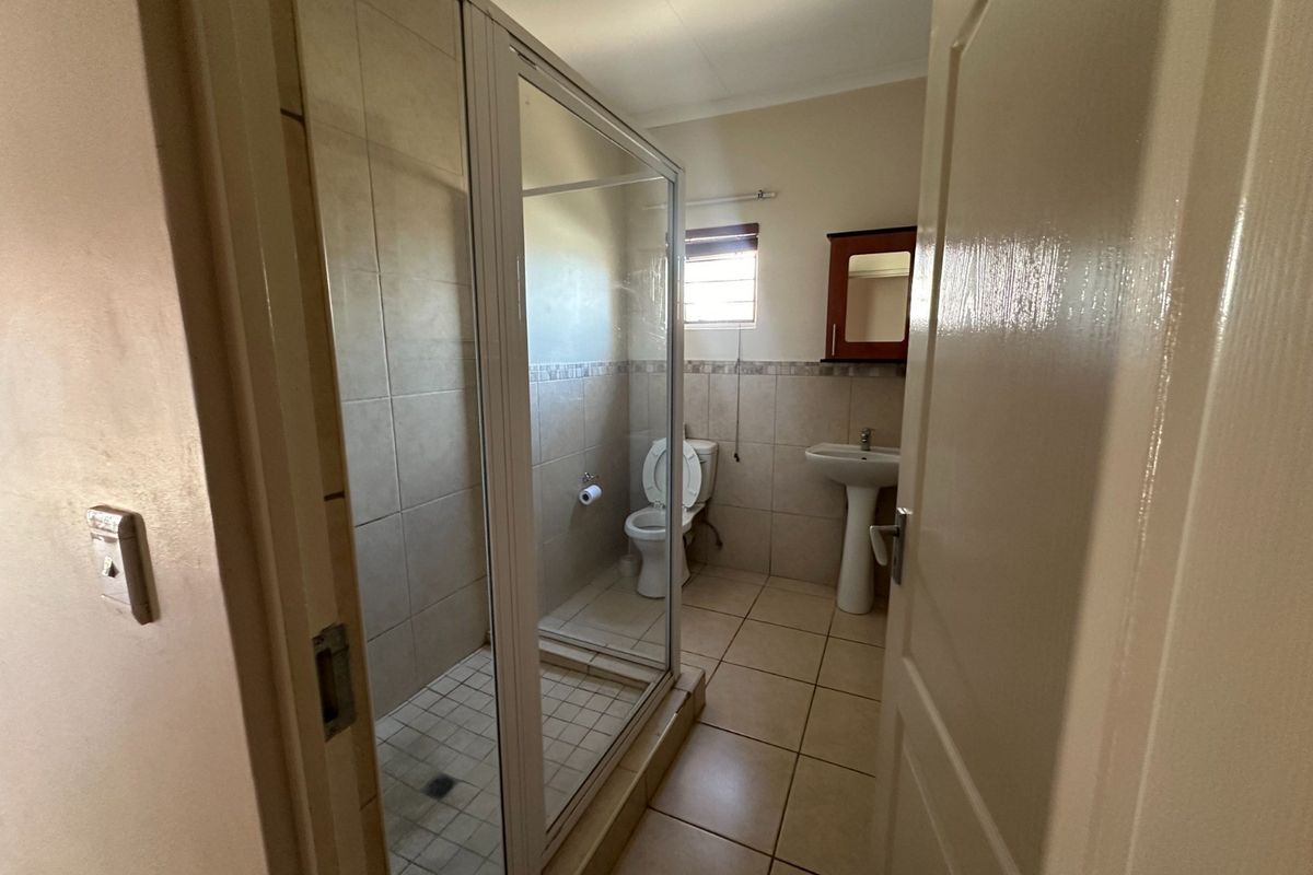 A functional bathroom featuring a glass-enclosed shower, pedestal sink, toilet, and neutral wall and floor tiling.