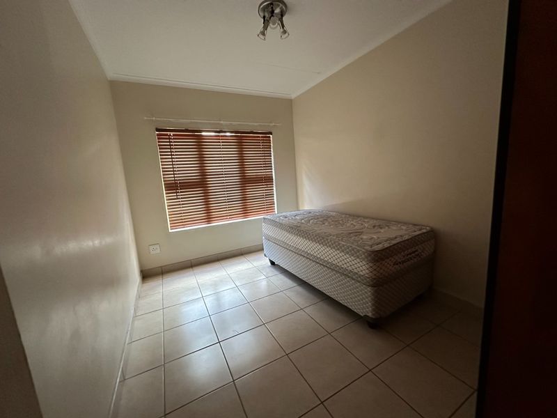 A simple bedroom featuring neutral wall paint, tiled flooring, and venetian blinds, providing a clean and functional space.