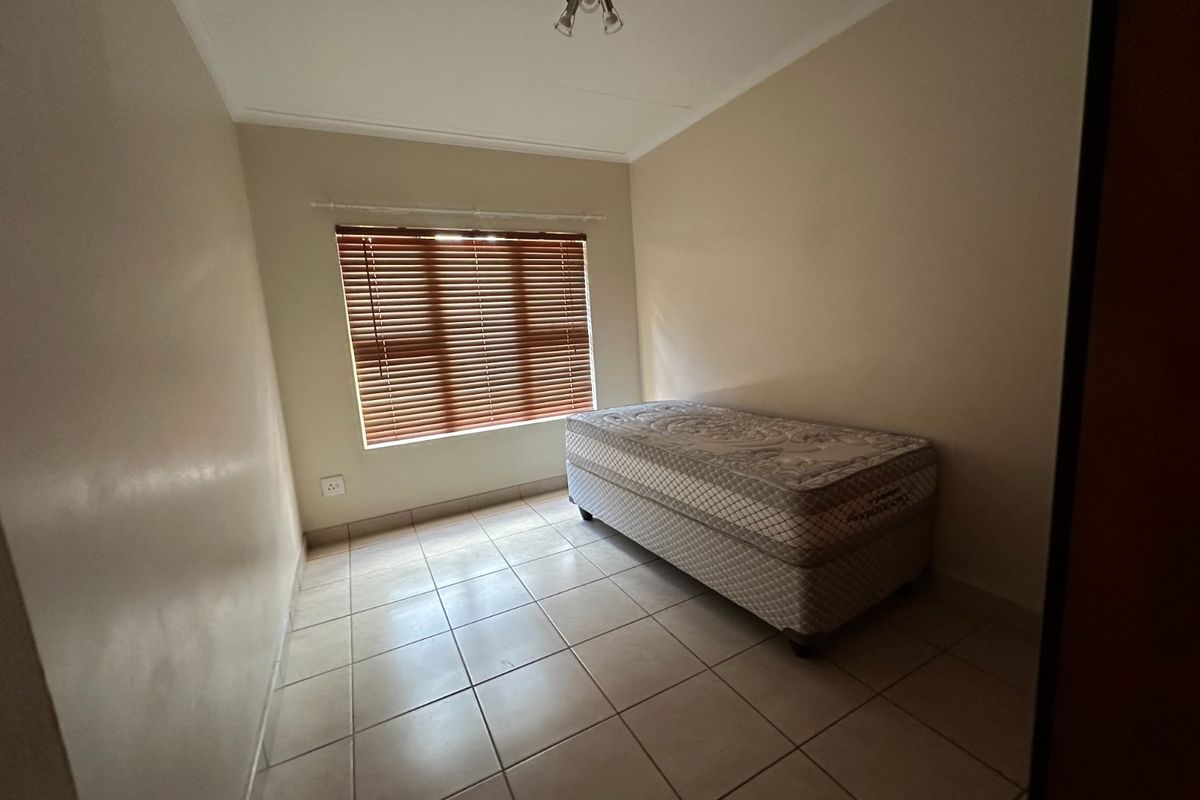 A simple bedroom featuring neutral wall paint, tiled flooring, and venetian blinds, providing a clean and functional space.