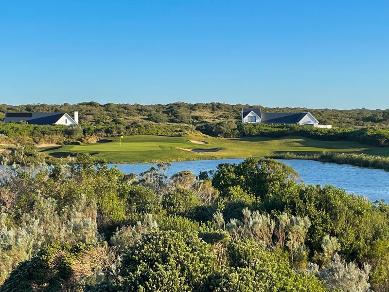 A scenic view overlooking a golf course green, water hazard, and surrounding natural landscape with residential properties in the distance.