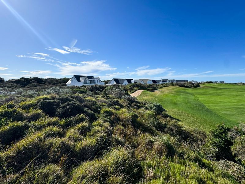 A scenic view overlooking a well-maintained golf course with surrounding coastal vegetation and residential properties in the distance.
