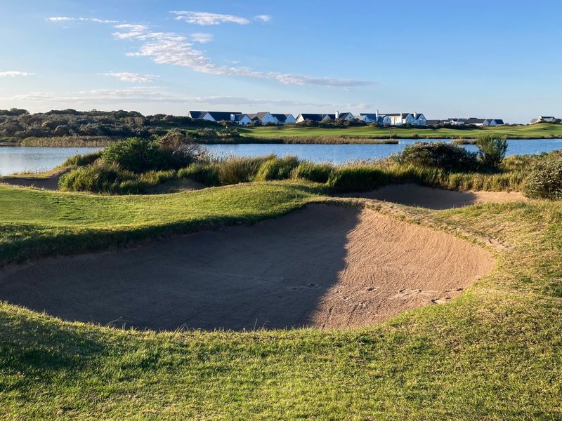 A scenic view of a golf course sand bunker overlooking a tranquil lake with residential properties in the background.