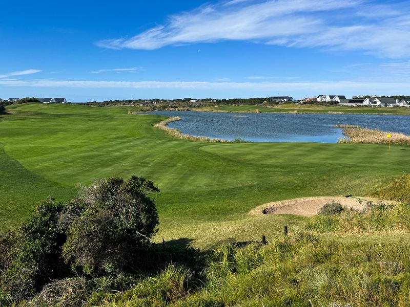 A scenic view overlooking a well-maintained golf course fairway, a large lake, and surrounding residential properties in the distance.