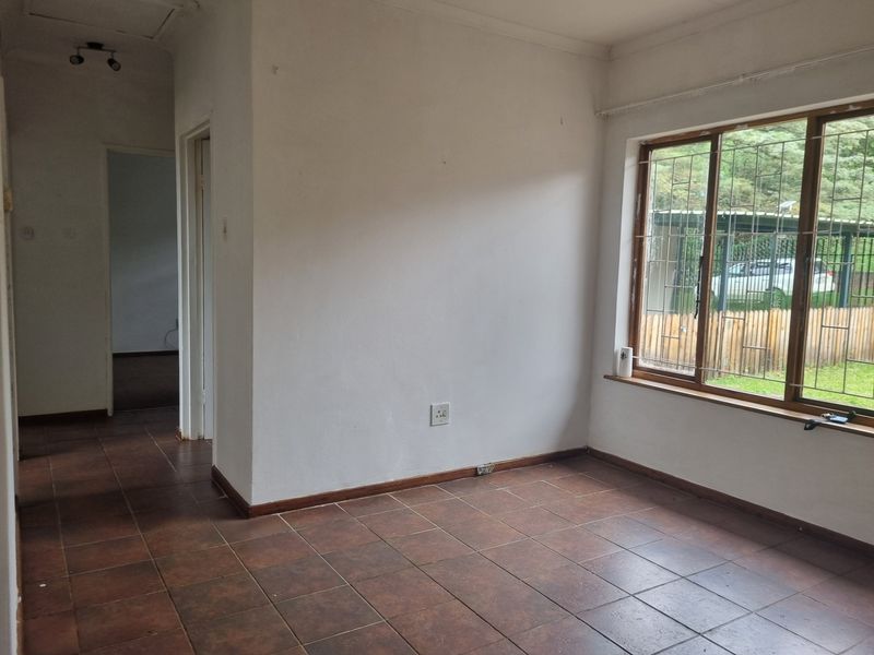 An empty living area featuring tiled flooring and a large window with security bars, providing a blank canvas for interior design.
