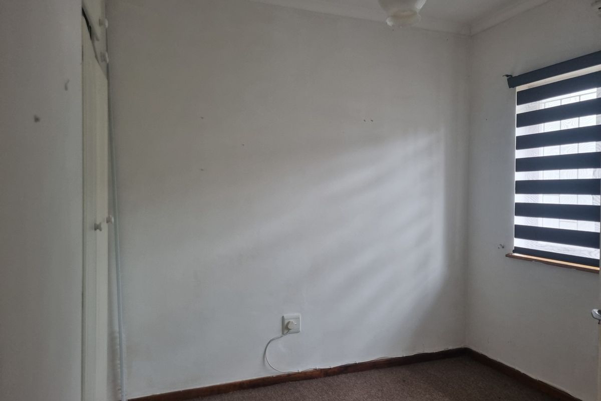 An empty bedroom featuring built-in cupboards, carpeted flooring, and a window with a zebra blind, requiring minor cosmetic updates.