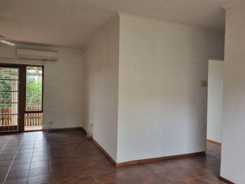 An empty living room featuring tiled flooring, an air conditioning unit, and a sliding glass door leading to an outdoor area.