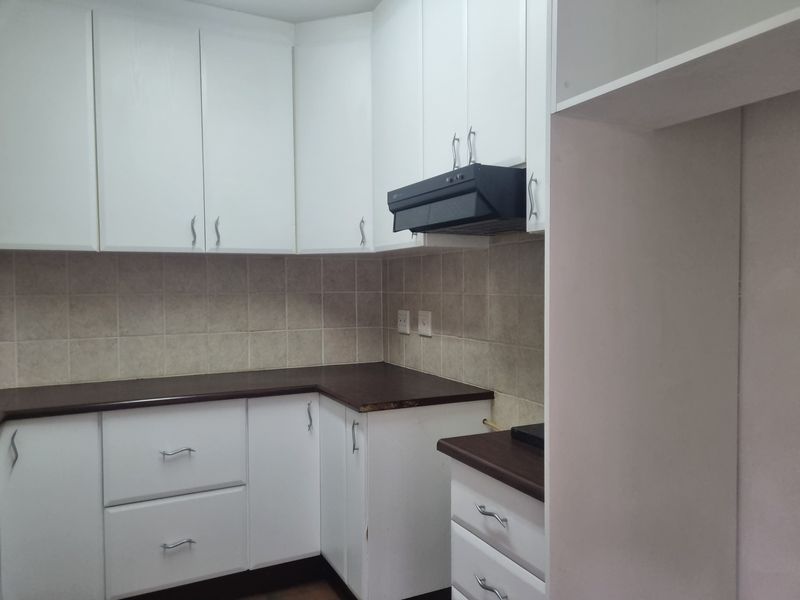 A functional kitchen featuring white cabinetry, dark laminate countertops, a tiled backsplash, and a built-in extractor fan.