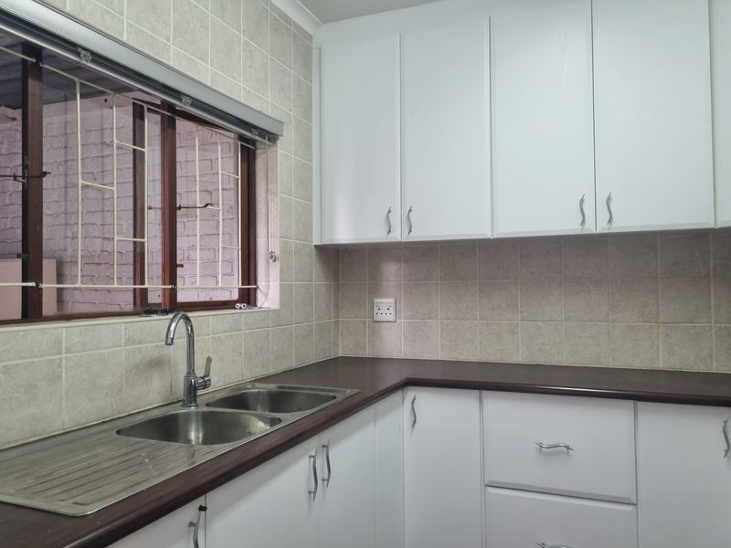 A clean kitchen featuring white cabinetry, a dark laminate countertop, a double bowl stainless steel sink, and neutral tiled backsplash.