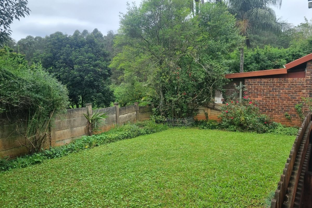 A private rear garden featuring a lawn area, enclosed by a combination of brick, precast concrete, and timber fencing with established surrounding trees.