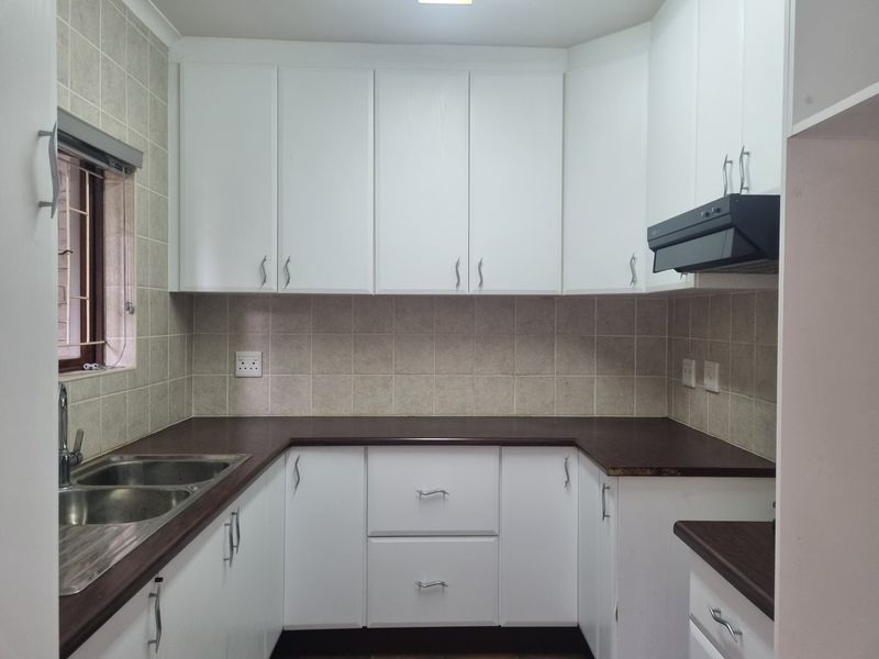 A functional kitchen featuring white cabinetry, dark laminate countertops, a stainless steel double sink, and a tiled backsplash.