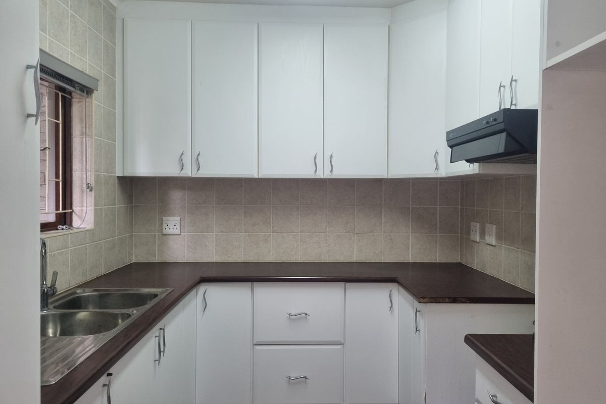 A functional kitchen featuring white cabinetry, dark laminate countertops, a stainless steel double sink, and a tiled backsplash.