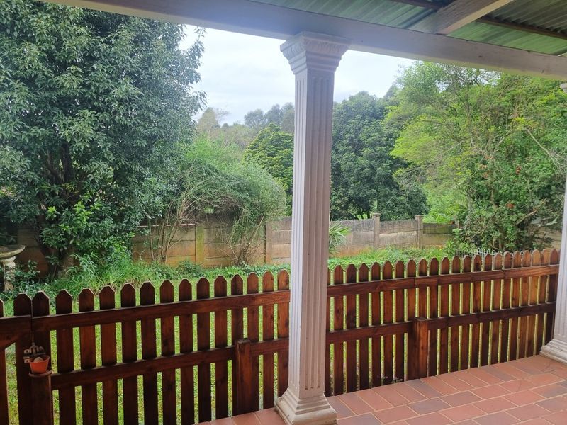 A covered patio area featuring tiled flooring and a decorative column, overlooking a private garden with a timber fence and mature trees.
