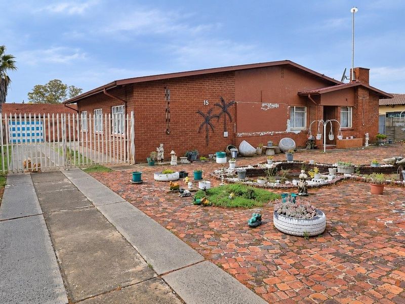 Rear exterior view of a brick house featuring a paved courtyard, perimeter walling, and a gated driveway entrance.