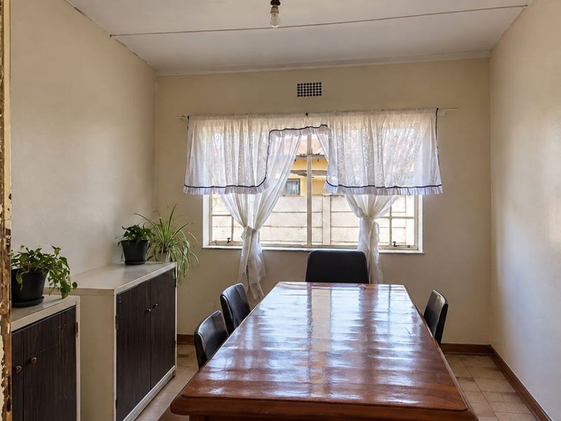 A functional dining room featuring tiled flooring, a window with security bars, and built-in storage cabinetry, offering a blank canvas for renovation.