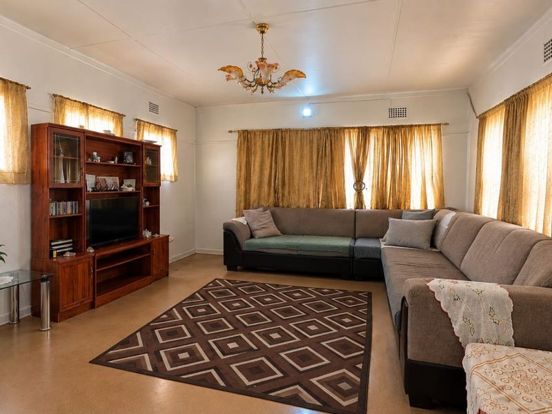 A spacious living room featuring neutral walls, large windows with curtains, and a central ceiling light fixture.