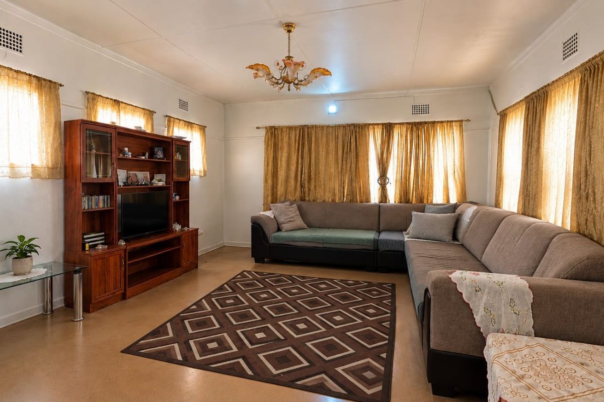 A spacious living room featuring neutral walls, large windows with curtains, and a central ceiling light fixture.