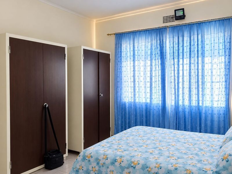 A bedroom featuring built-in cupboards and large windows with curtain rails, providing a functional space with neutral wall finishes.