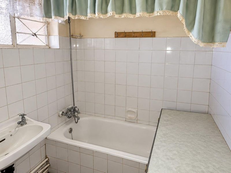 A dated bathroom featuring a built-in bathtub, wall-mounted basin, and tiled walls, offering significant potential for a modern renovation.