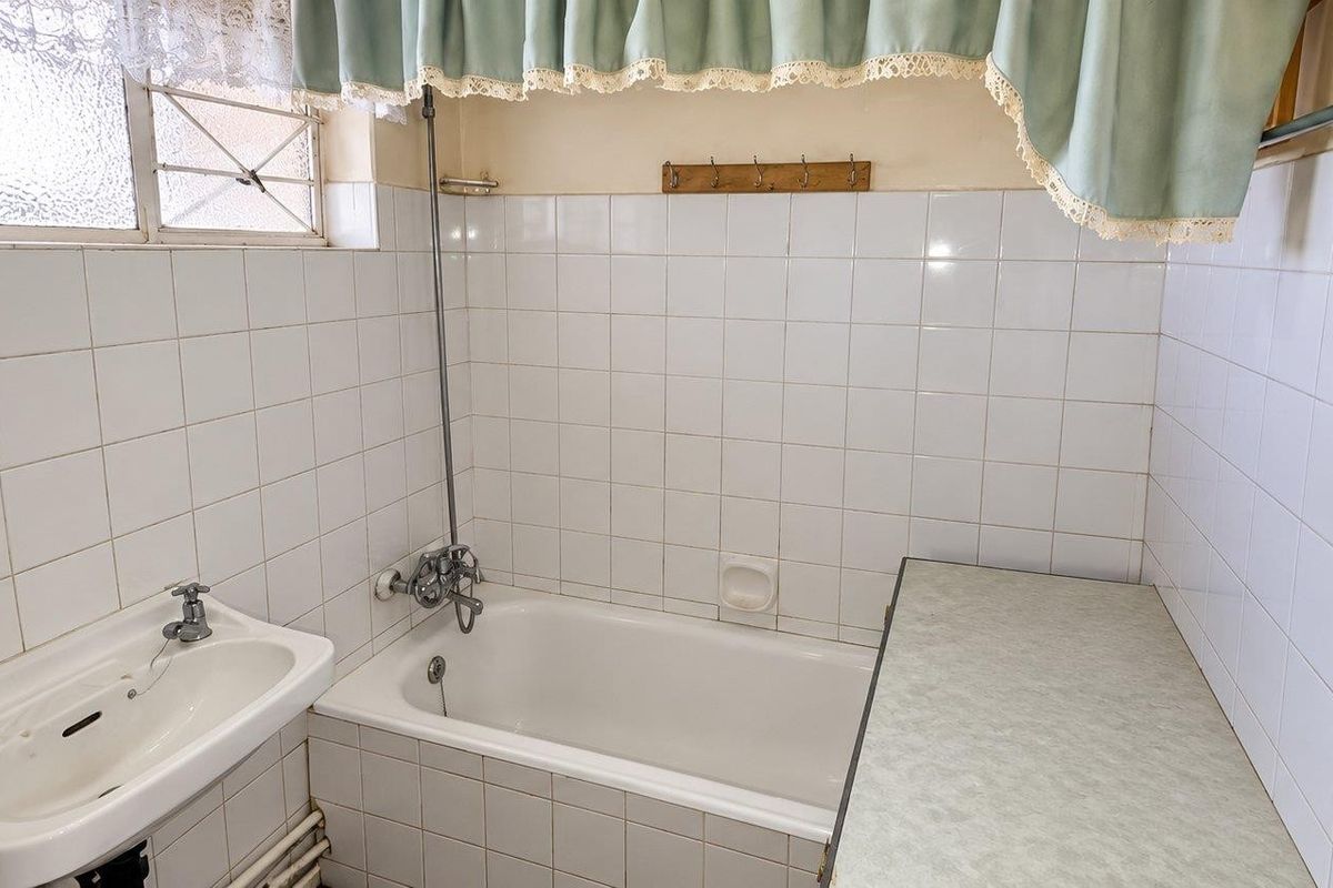 A dated bathroom featuring a built-in bathtub, wall-mounted basin, and tiled walls, offering significant potential for a modern renovation.