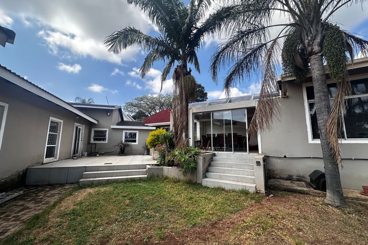 Rear exterior view featuring a tiled patio area, concrete steps, and an enclosed glass-fronted patio structure set within a garden space.