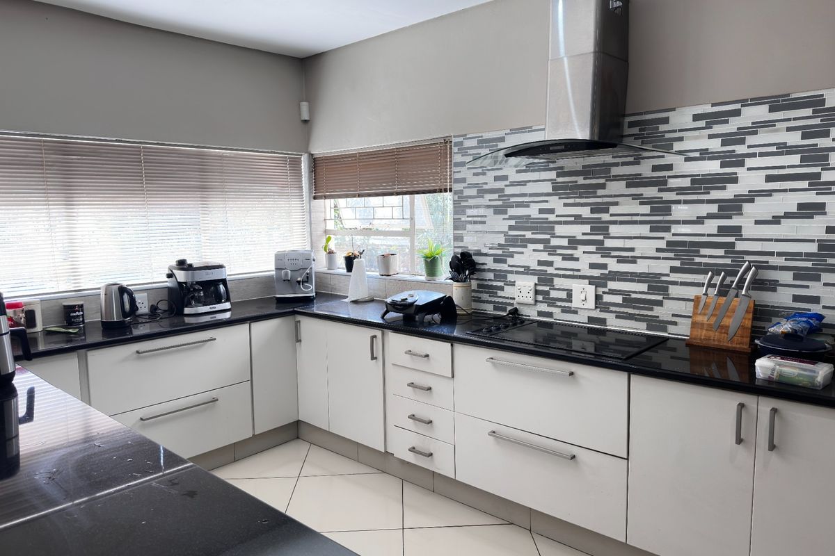 Modern kitchen featuring sleek white cabinetry, black granite countertops, a striking mosaic tile backsplash, and a stainless steel extractor fan.